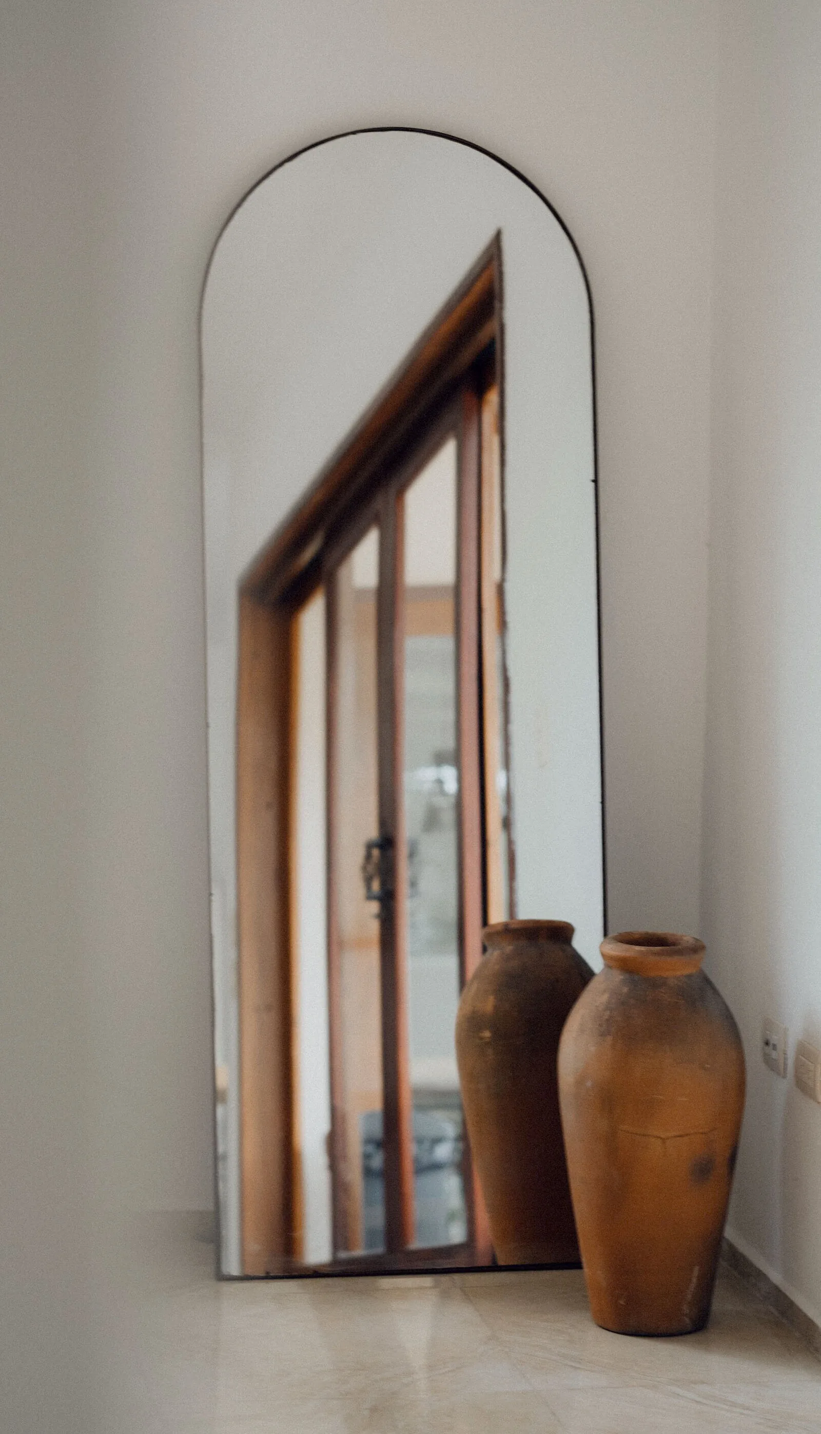 Arched mirror leaning against a warm plaster wall
